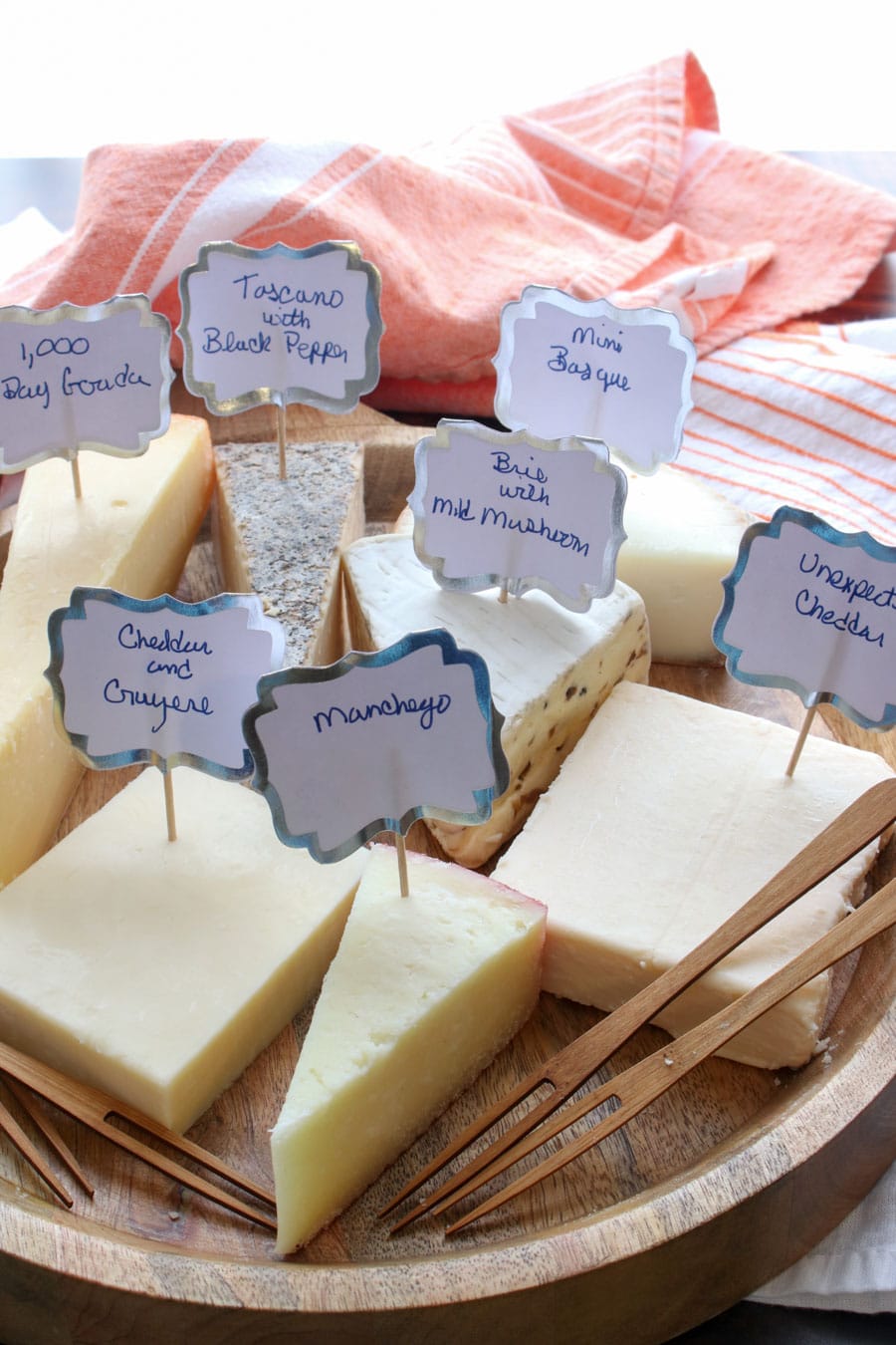 board with seven unwrapped cheeses with labels telling what they are