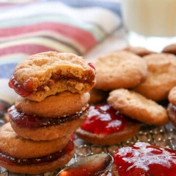 a stack of peanut butter and jelly cookies and a spoon of jelly on a cookie rack