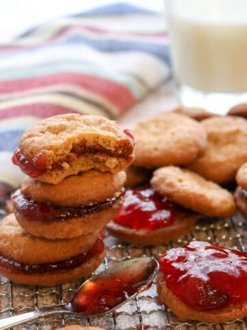 a stack of peanut butter and jelly cookies and a spoon of jelly on a cookie rack