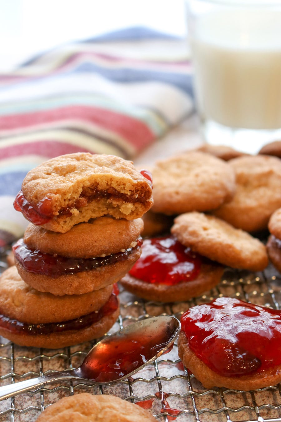 a stack of peanut butter and jelly cookies and a spoon of jelly on a cookie rack