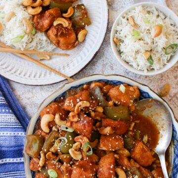 Serving bowl filled with cashew chicken with rice in a bowl on the side