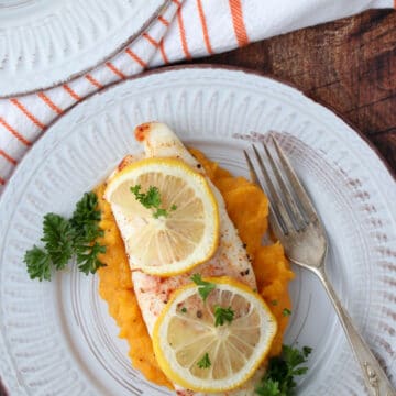 A piece of fish topped with lemon slices sitting on top of butternut squash puree
