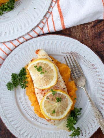 A piece of fish topped with lemon slices sitting on top of butternut squash puree