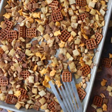 Chex party mix on a cookies sheet being scooped with a metal spatula