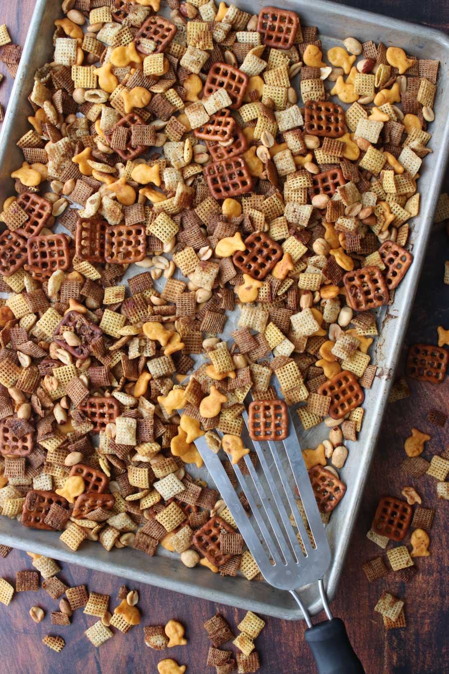 Chex party mix on a cookies sheet being scooped with a metal spatula