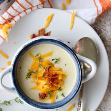 close up overhead shot of potato soup on a plate with a spoon. Soup is topped with cheese, bacon and fresh thyme