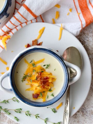 close up overhead shot of potato soup on a plate with a spoon. Soup is topped with cheese, bacon and fresh thyme