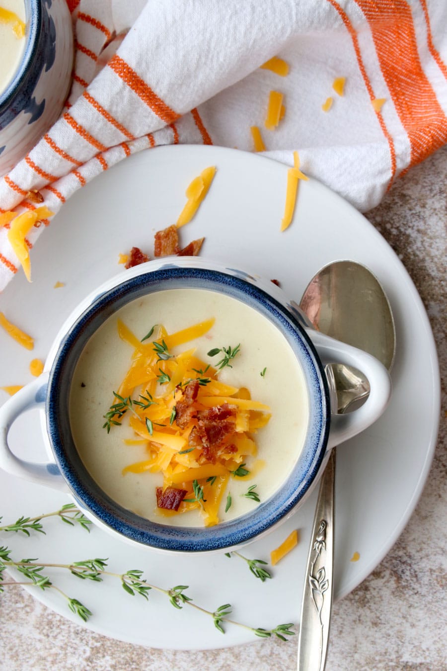 close up overhead shot of potato soup on a plate with a spoon. Soup is topped with cheese, bacon and fresh thyme