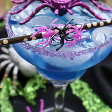 Blue cocktail with a black and white straw and a purple toy spider sitting on top