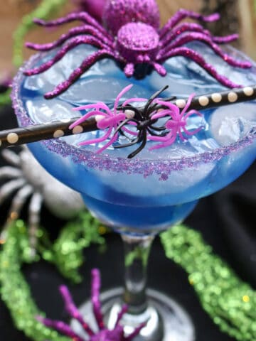 Blue cocktail with a black and white straw and a purple toy spider sitting on top