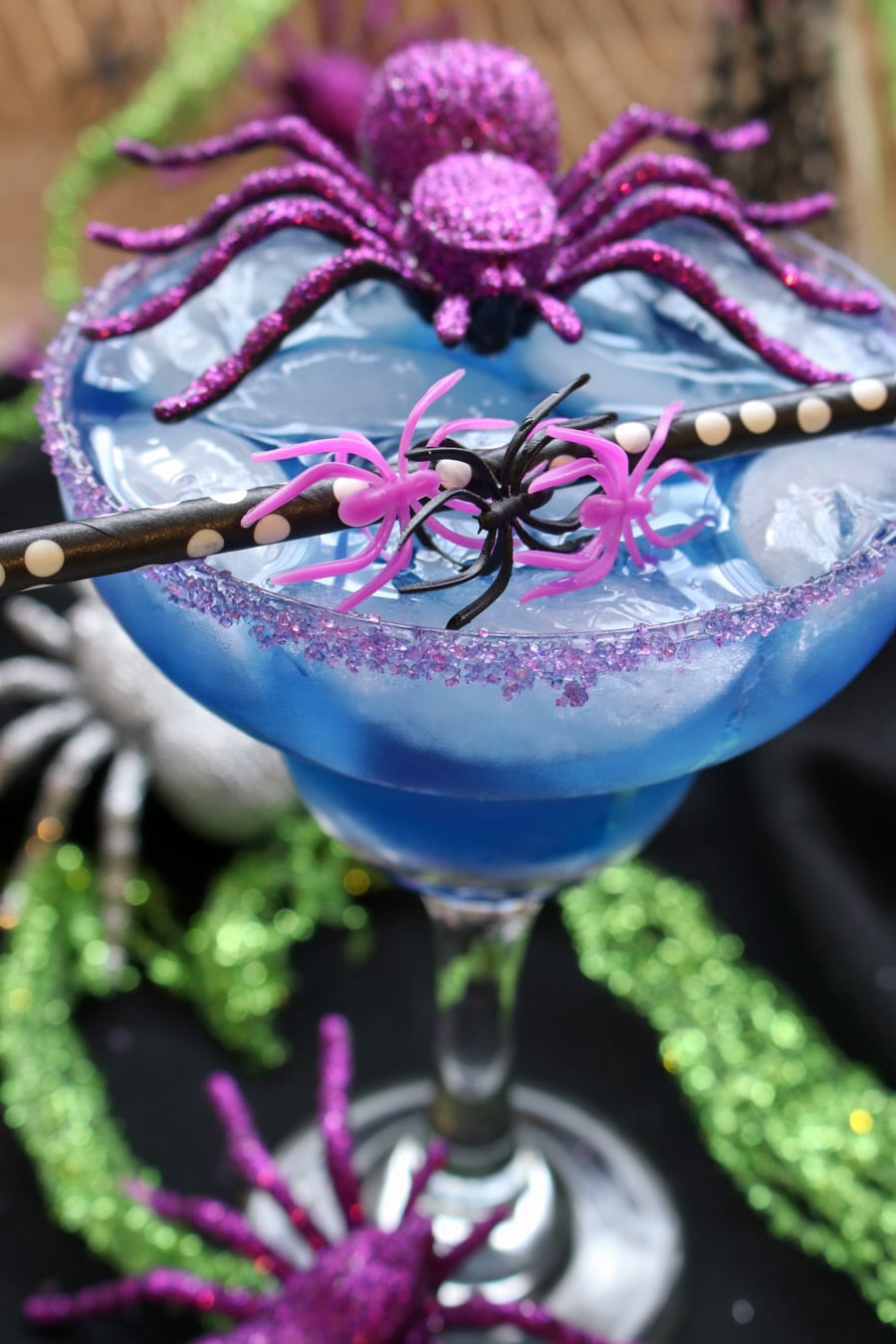 Blue cocktail with a black and white straw and a purple toy spider sitting on top