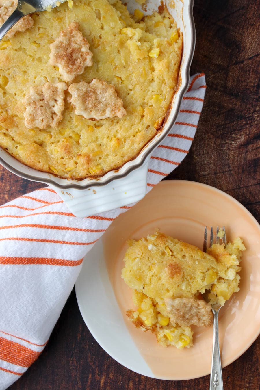 a dish of corn pudding sitting next to the full casserole of corn pudding