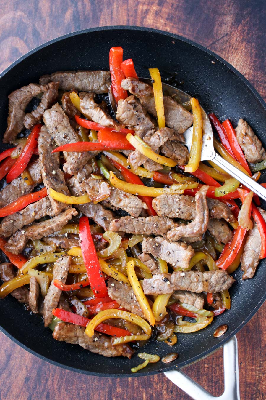 Skillet filled with beef strips and red and yellow bell peppers