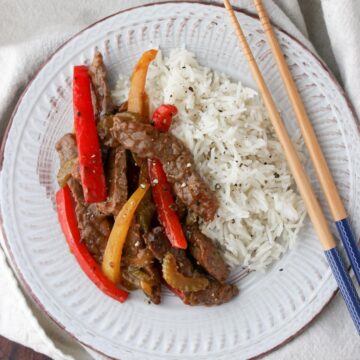 White plate with beef, red and yellow bell pepper slice, with side of rice and chop sticks