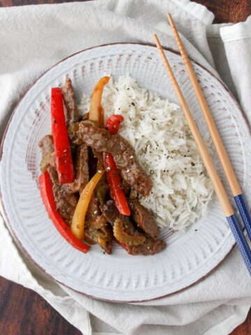 White plate with beef, red and yellow bell pepper slice, with side of rice and chop sticks