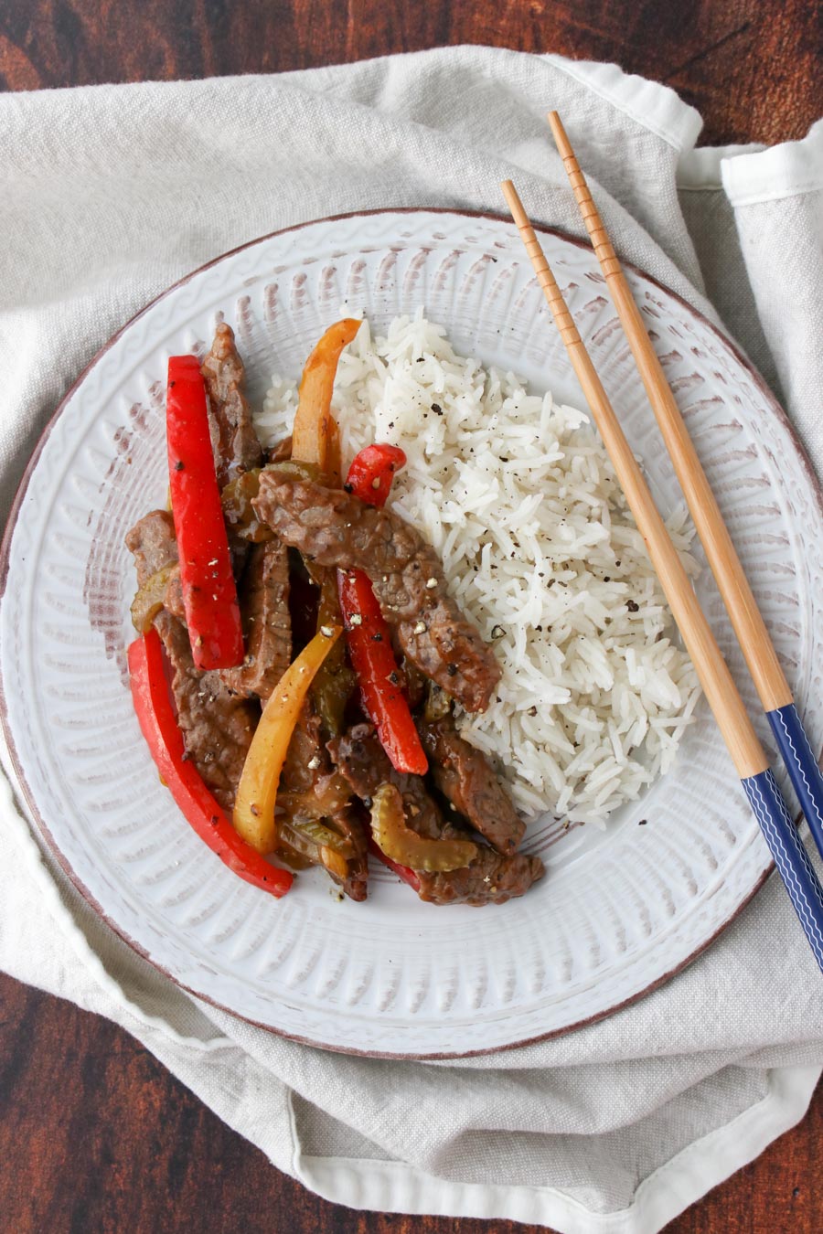 White plate with beef, red and yellow bell pepper slice, with side of rice and chop sticks