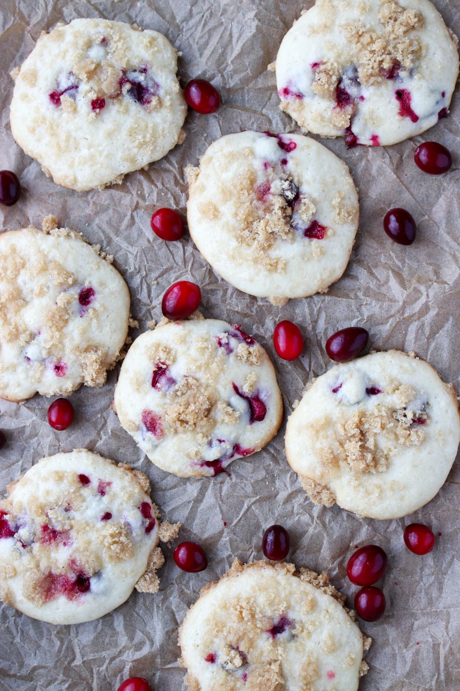 Muffin top cookies on a brown piece of paper along with fresh cranberries