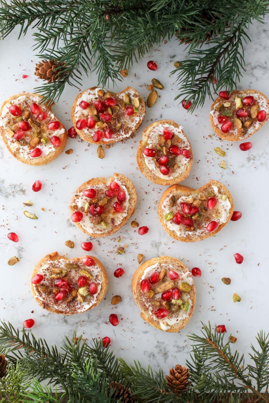 Pistachio Pomegranate Crostini  on a marble background with greens on top and bottom