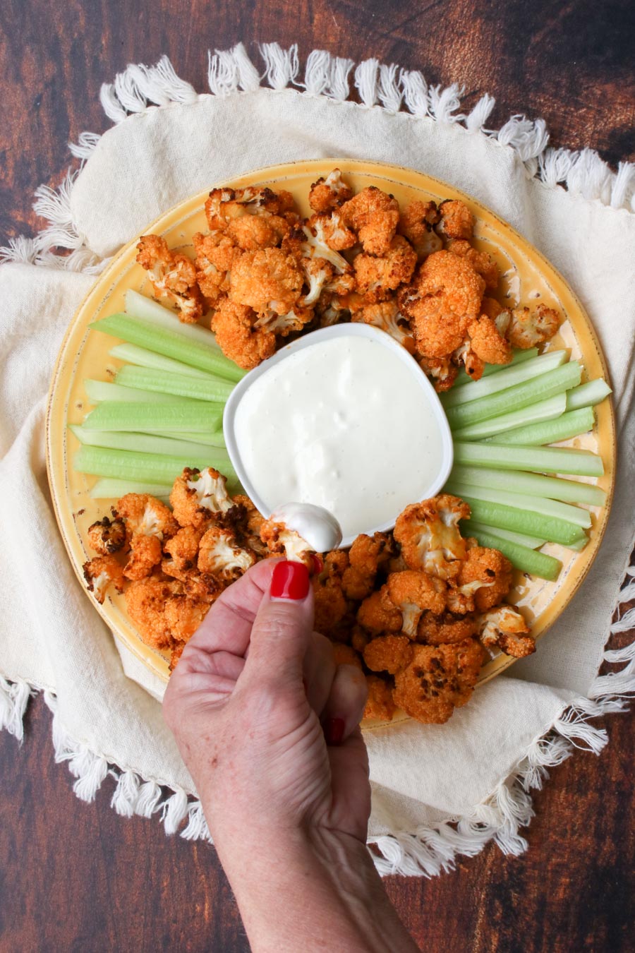 Woman's hand with red finger nails holding piece of buffalo cauliflower dipped in blue cheese dressing