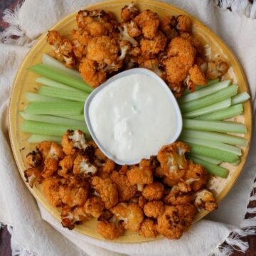 yellow plate with buffalo cauliflower and celery with blue cheese dip in the middle