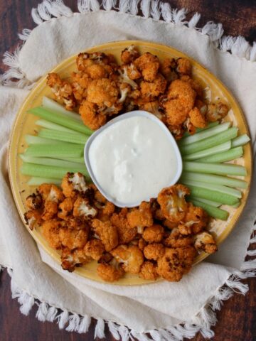 yellow plate with buffalo cauliflower and celery with blue cheese dip in the middle