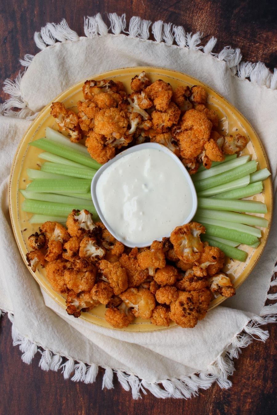 yellow plate with buffalo cauliflower and celery with blue cheese dip in the middle