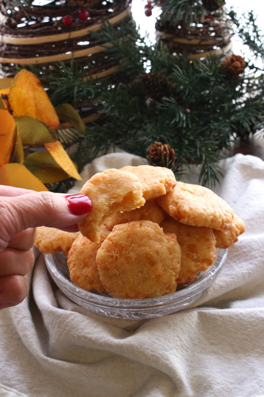 Woman's hand holding a cheddar cheese shortbread in front of a bowl of them