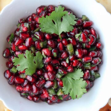 white bowl filled with pomegranate and three cilantro leaves