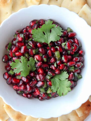 white bowl filled with pomegranate and three cilantro leaves