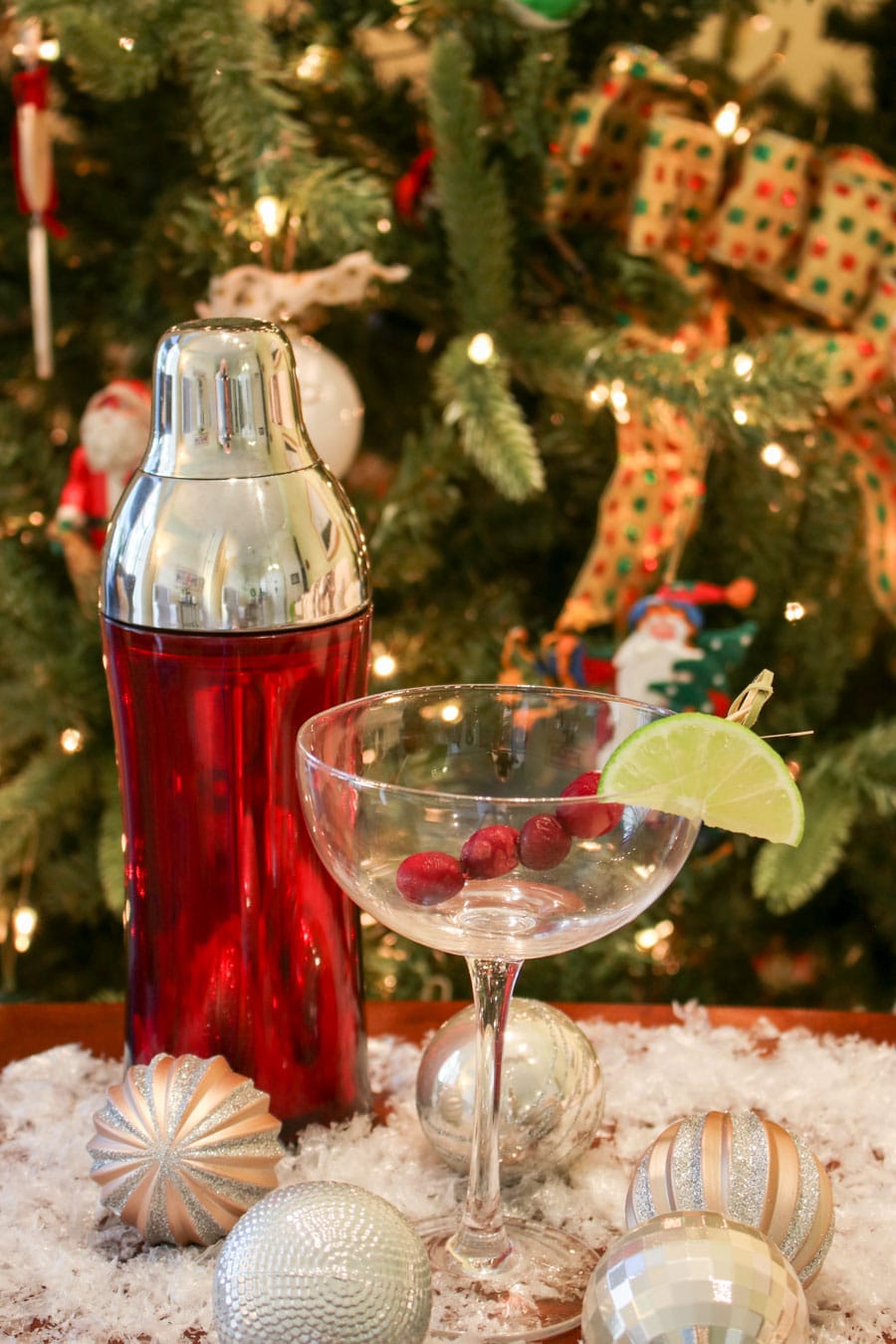 empty martini glass with a red shaker next to it. Christmas tree in the background.