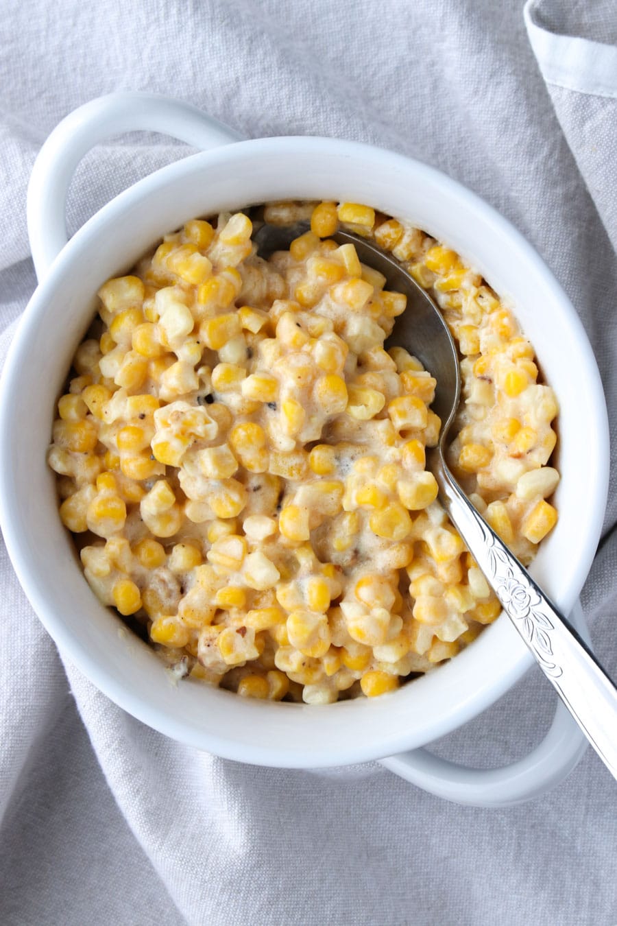 white bowl filled with creamed corn with a serving spoon on a gray napkin