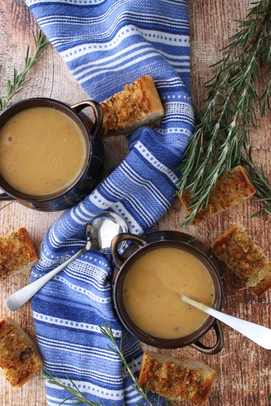 2 bowls of soup with a blue napkin and fresh rosemary sprigs and garlic toast