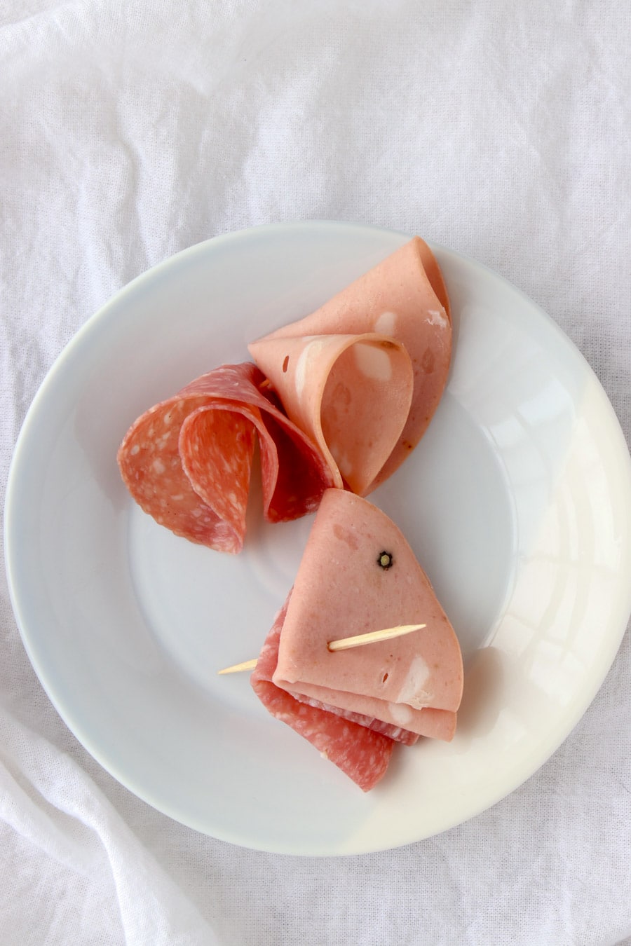 plate with mortadella and salami slices held together by a tooth pick