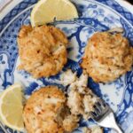 blue and white plate with three crab cakes, two slices of lemon and fork