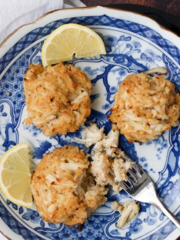 blue and white plate with three crab cakes, two slices of lemon and fork