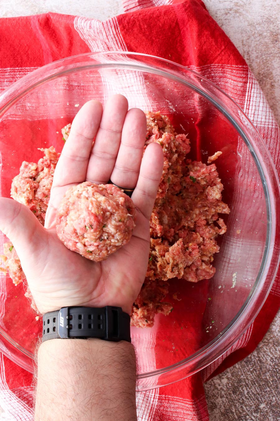 Man's hand holding a large raw meatball