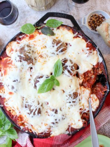 cast iron skilled of baked meatballs and pasta covered in cheese