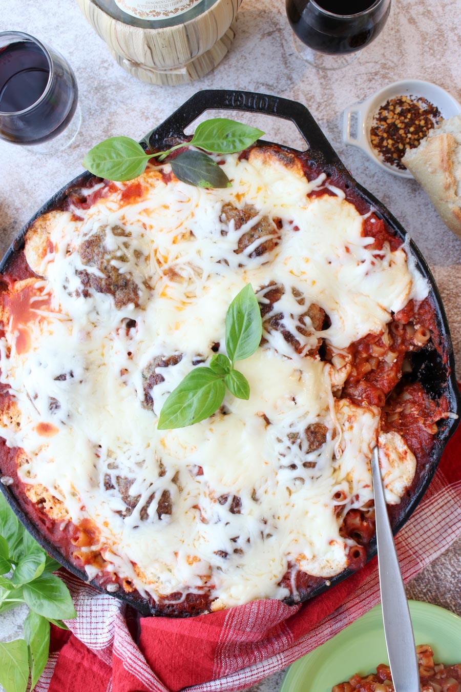 cast iron skilled of baked meatballs and pasta covered in cheese