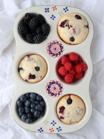 Pretty ceramic muffin plate with three muffins. blueberries, raspberries, blackberries