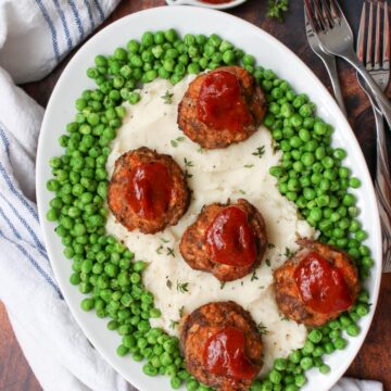 platter of mashed potatoes, surrounded by green peas and topped with mini meatloaf meatballs