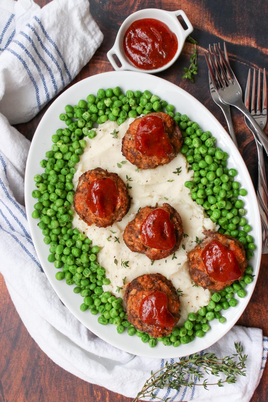 platter of mashed potatoes, surrounded by green peas and topped with mini meatloaf meatballs