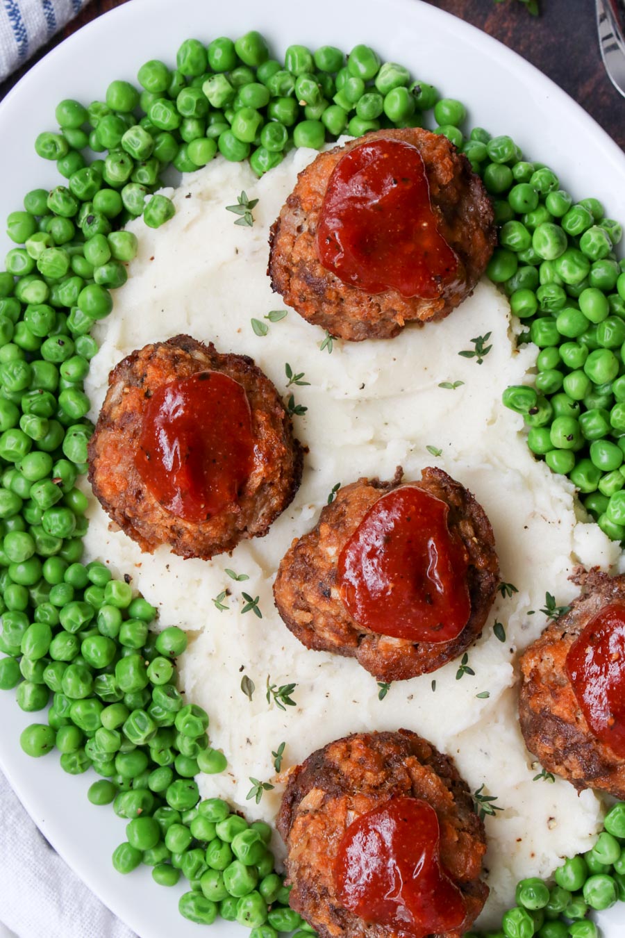 close of shot of platter with mashed potatoes, peas, and mini meatloaves