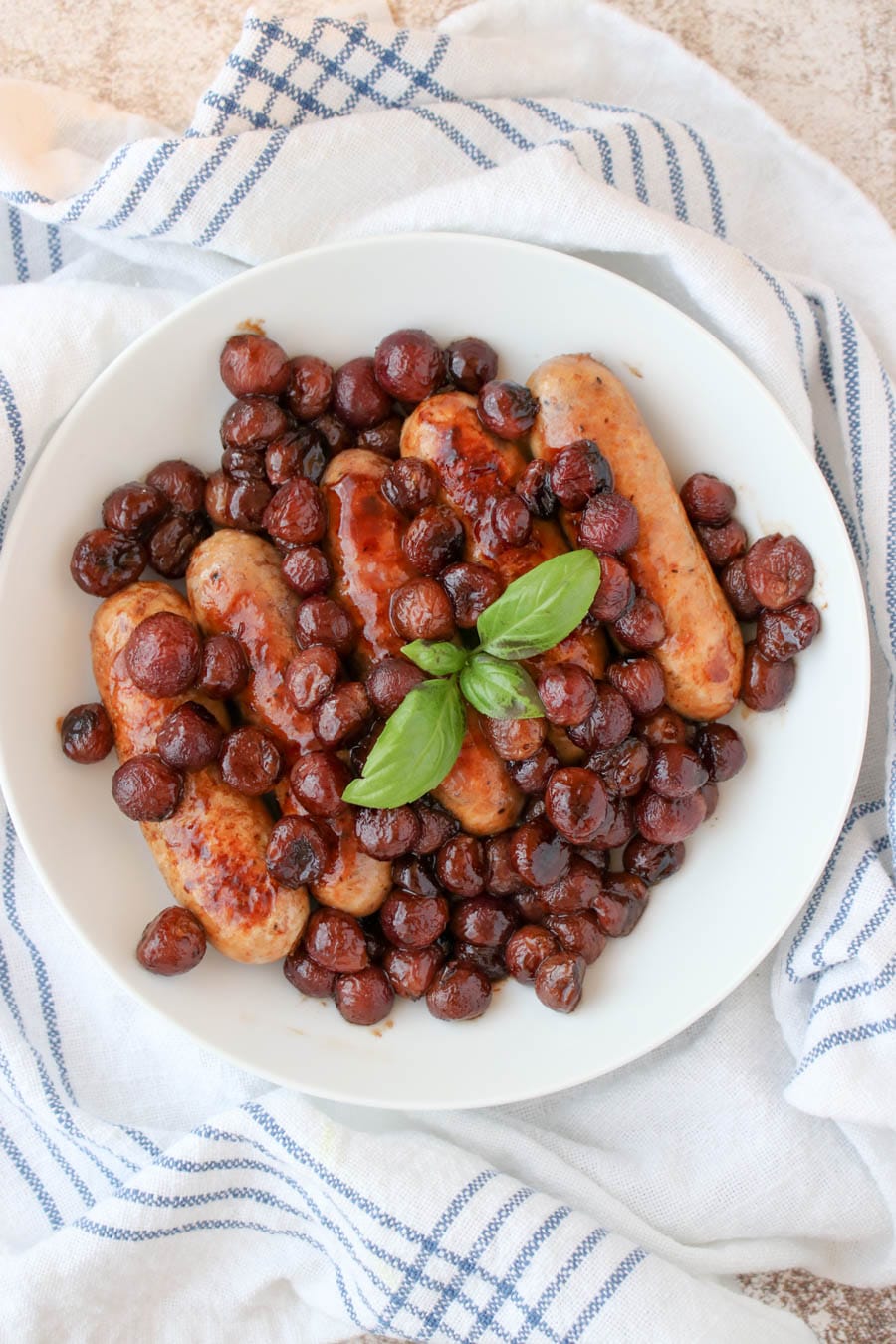 a white plate with cooked sausages, grapes and a sprig of fresh basil 