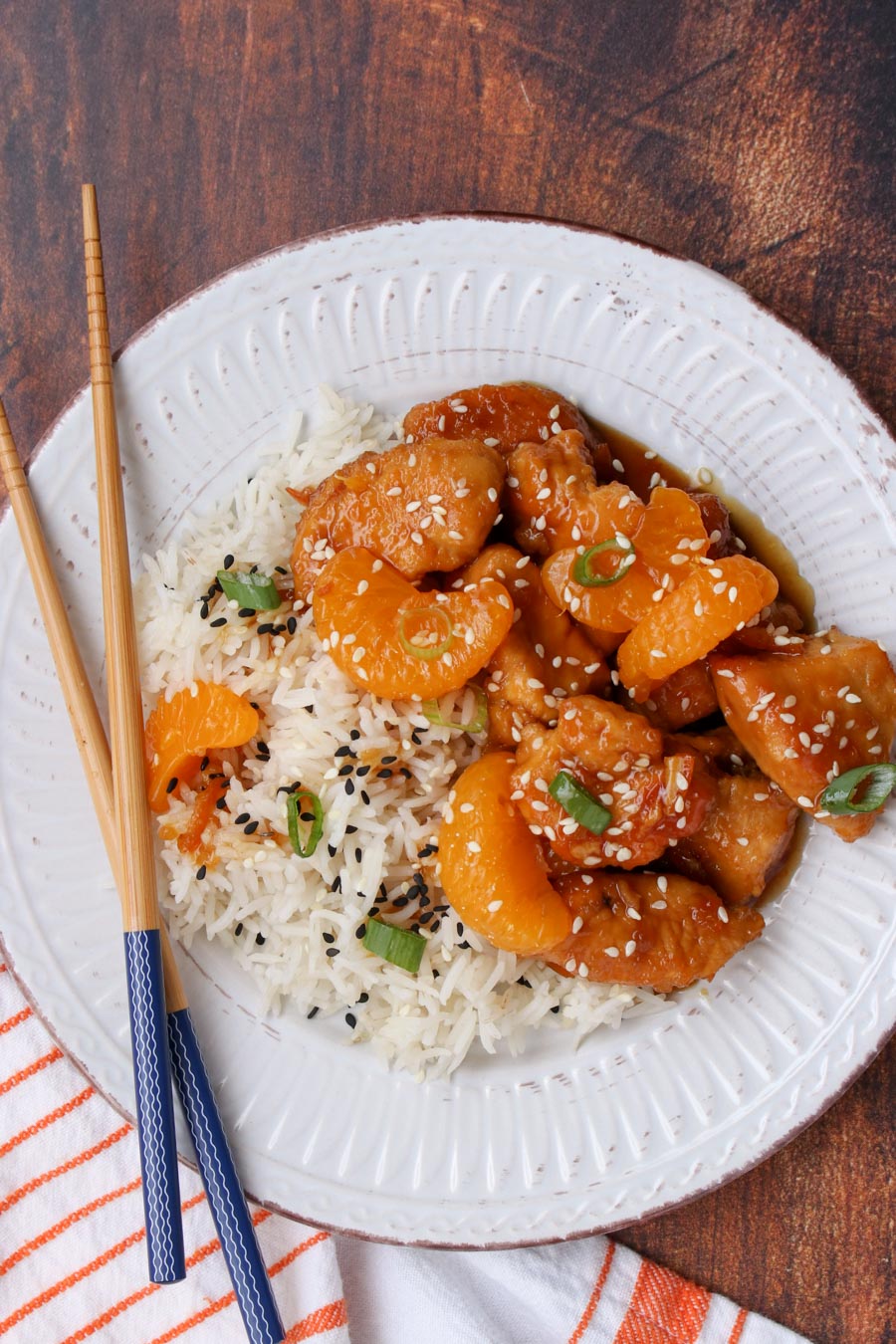 white plate with orange chicken and rice and chop sticks