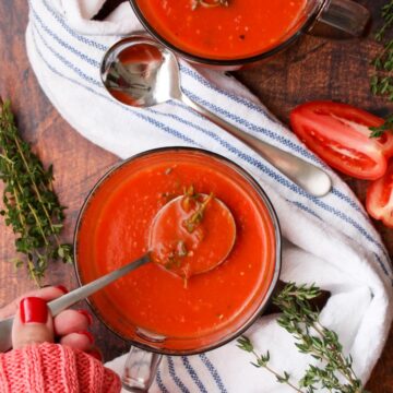 Ladies hand with a spoon of tomato soup next to another bowl of soup and a blue and white cloth