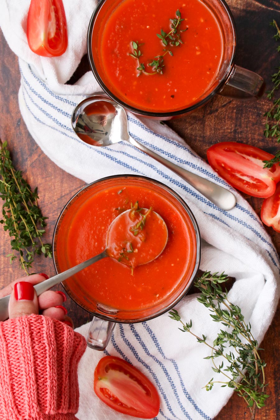 Ladies hand with a spoon of tomato soup next to another bowl of soup and a blue and white cloth