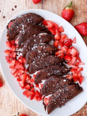 a platter of chocolate tacos surrounded by diced strawberries