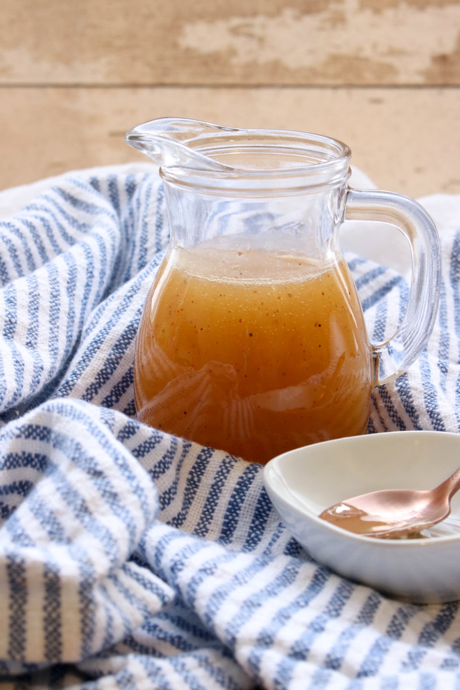 jar of bourbon butter sauce, small white dish with a gold spoon in it, all on a blue and white cloth 