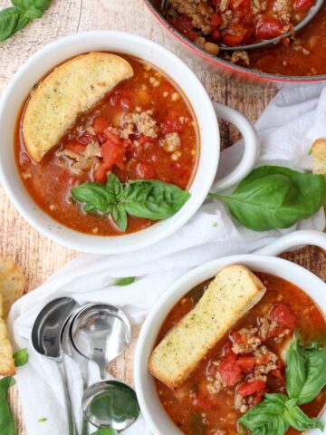 two bowls of sausage and bean soup with large croutons