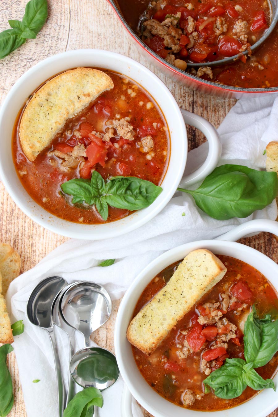 two bowls of sausage and bean soup with large croutons